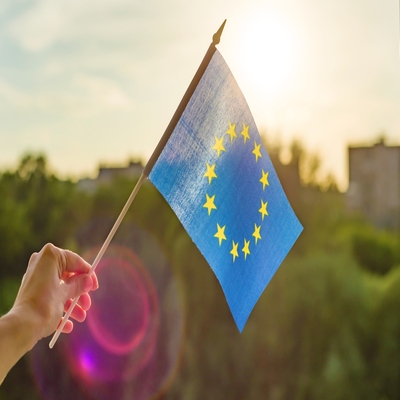 Hand holds European Union flag in an open window. Background blue sky, silhouette of the city, sunset.
